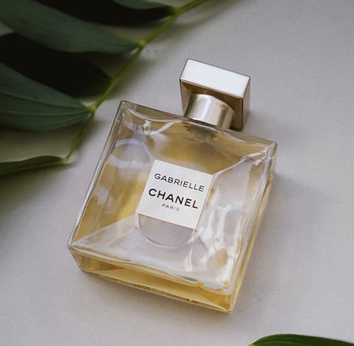 Gabrielle Essense perfume bottle laying flat on a table with green leaves above and below it.